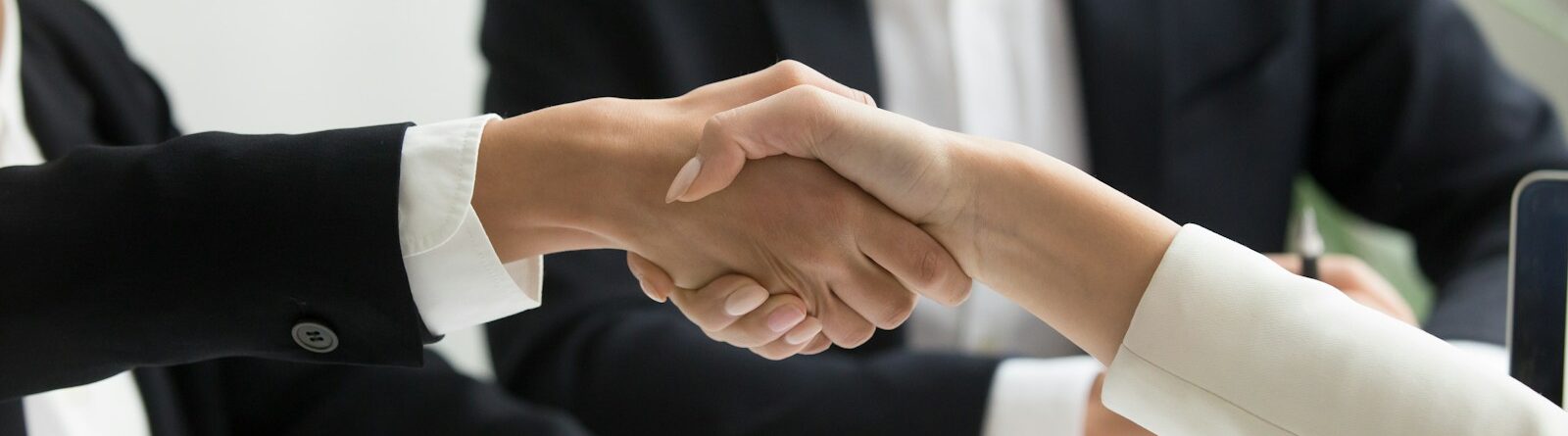 two people shaking hands in front of a laptop